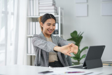 Businesswoman doing stretch exercise at desk in bright modern office, smiling and relaxed.