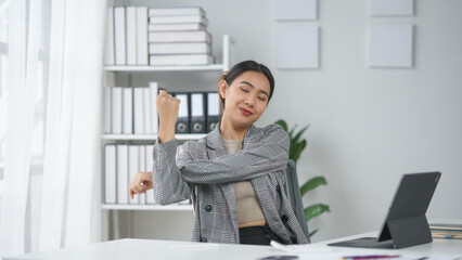 Businesswoman stretching and relaxing at desk in modern office, illustrating workplace wellness and productivity in a peaceful environment.