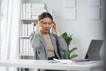 Businesswoman stressed and frustrated at desk in office, holding head. Young professional with headache, work stress concept.