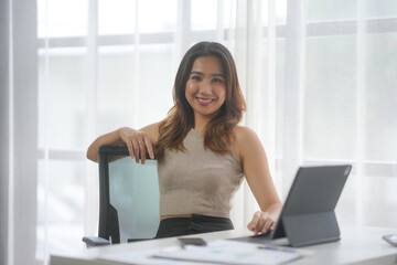 Confident businesswoman smiling at desk with laptop and documents in bright office setting, professional work environment.