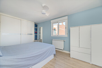 Bedroom with white furniture, desk with swivel chair, matching wardrobes, white aluminum and glass windows and blue painted walls