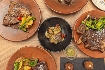 Top view image of various plates of different cuts of grilled beef along with barbecue wings in sauce