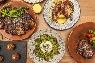 Top view image of various plates of different cuts of grilled beef together with a burrata salad and a plate with octopus