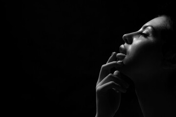 A black and white portrait of a woman, captured in dramatic lighting. The light highlights her profile, creating a sense of mystery and intrigue, copy space