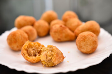 Coxinhas pequenas em um prato branco com fundo desfocado com duas delas abertas mostrando o recheio de frango salgadinho