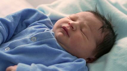 Close-up of a newborn baby peacefully sleeping in a blue onesie, highlighting the delicate features and serene expression, capturing the pure and tranquil moments of early life in a hospital setting