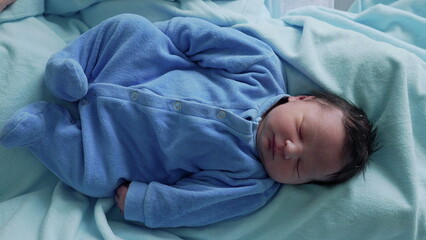 Full-body view of a newborn baby sleeping in a blue onesie on a soft, light blue blanket. This photo emphasizes the peacefulness and purity of a newborn's sleep in a safe and comfortable environment