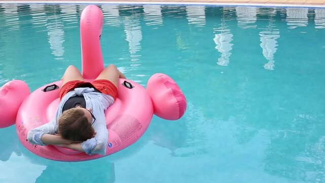 Woman on flamingo pool float  in pool in hotel. Summer holidays, enjoying summer vacations during quarantine. 
