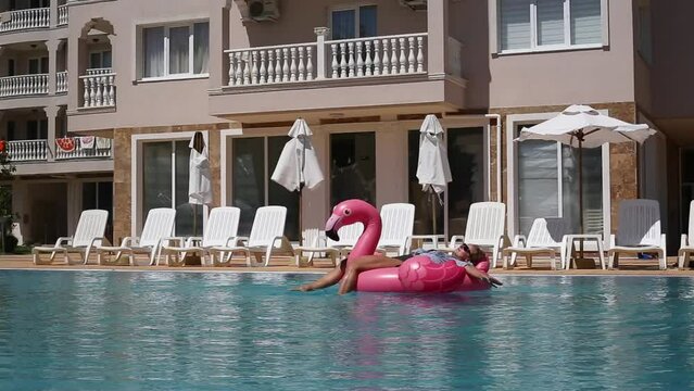 Beach vacation woman relaxing in pool float flamingo inflatable ring with unicorn floating on turquoise pool water
