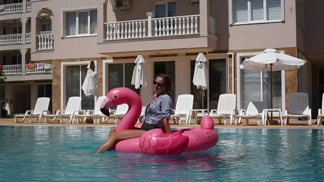 Beach vacation woman relaxing in pool float flamingo inflatable ring with unicorn floating on turquoise pool water
