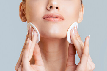 This image shows a woman applying cotton rounds to her face as part of her skincare routine. She is...