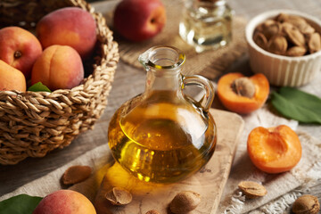 Apricot kernel oil in a glass jug on a table with fresh apricots in a wicker basket