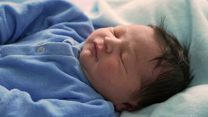 Newborn baby sleeping soundly in a blue onesie, nestled in a cozy blanket, capturing the serene and peaceful early moments of life, emphasizing innocence and tranquility in a home environment