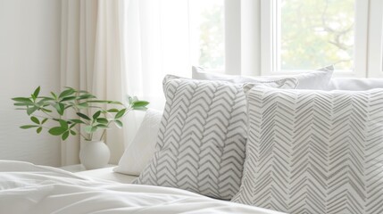 A close-up image of a white and grey chevron patterned pillow on a bed. The bed is made with white sheets and is next to a window