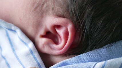 Newborn baby sleeping on the mother's chest, wrapped in a blue and white striped shirt. The image...