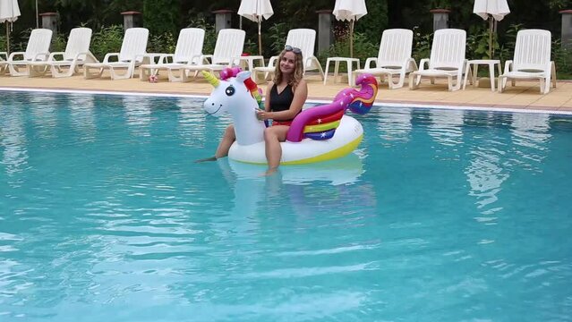 young beautiful woman in swimsuit on inflatable unicorn pool float in pool in the hotel. Summer holidays
