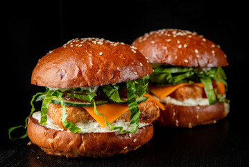Two gourmet burgers with sesame buns, fresh greens, cheese, and sauce on a dark background