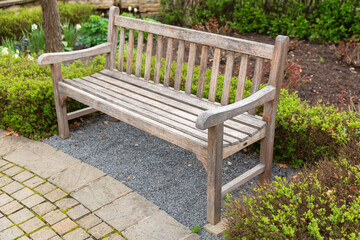 An empty wooden park bench stands on a paved ground
