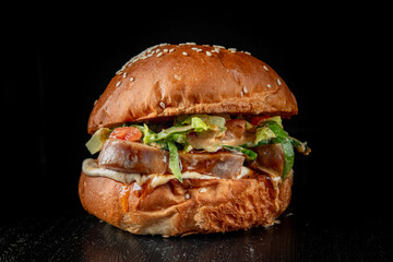 Close-up of a juicy burger with fresh lettuce and sauce on a sesame seed bun against a dark background