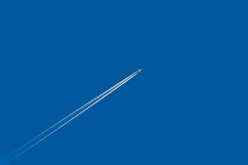 Airplane flying in the blue sky, leaving a white trail behind it.