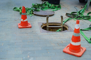 sewer manhole with a ladder lowered into it, enclosed by special cones on the sidewalk, ensuring...