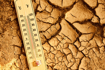 Climate change concept. Thermometer on arid, cracked soil representing extreme heat and drought...