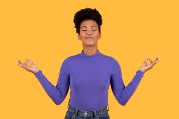 This image shows a woman with dark curly hair wearing a purple shirt and blue jeans. She is...