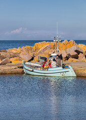 Decorative light green fishing boat anchored behind rocks on the Danish island Bornholm.