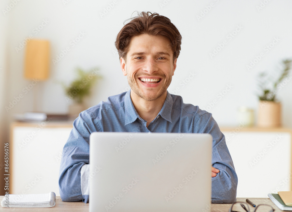 Poster a smiling man with crossed arms sits at a desk in an office, working on a laptop.