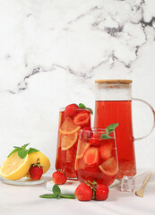 Iced strawberry tea or mint lemon smoothie is a refreshing summer drink recipe. Glass with berry fruit lemonade on a light concrete table, detox diet and weight loss concept, restaurant menu.