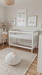 A modern nursery features a white crib with a white mattress against white walls and wooden flooring. Framed forest illustrations hang above the crib, with a white knitted pouf on a cream rug.