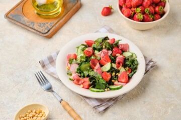 A healthy salad with cabbage kale, fresh cucumbers, radish, strawberries and smoked meat on a beige ceramic plate on a light concrete background.