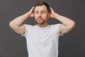 Cute bearded man massaging his scalp on gray background in studio, beauty and care concept