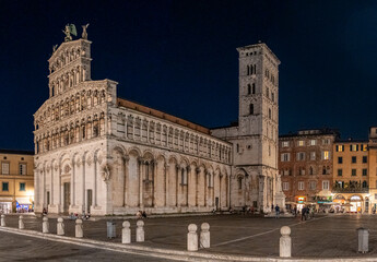 Obraz premium Night view of the San Michele in Foro church in Lucca, Italy, with surrounding buildings and a clear sky.