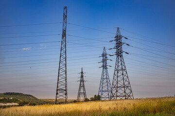 Three tall power lines are in a field with a blue sky