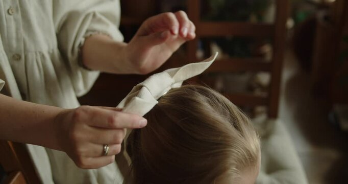 Young loving mother tying a hair bow for her adorable little daughter at home. Close-up slow motion shot.