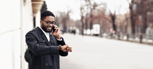 African American manager in formal outfit have phone conversation outdoors, standing by modern building on the street, checking time on watch, panorama with copy space