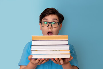 A very surprised teenage boy with glasses peeks out from behind a stack of books