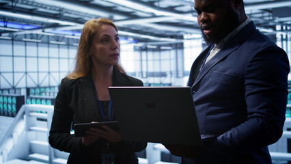 Team of IT specialists managing data center with advanced technology using devices. Coworkers in...