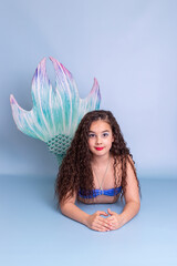 Beautiful child girl in a mermaid costume lie on light-blue background