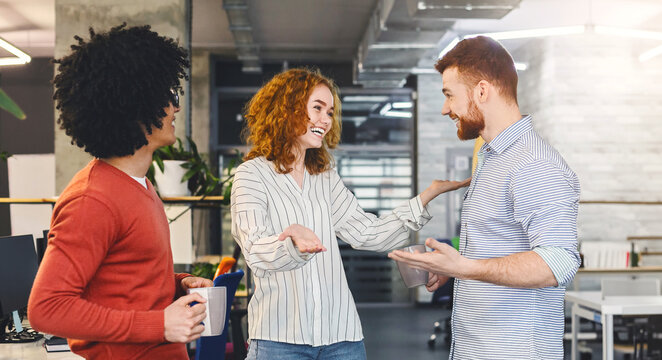 Very friendly girl hugging young man, welcoming new member of creative team in modern office