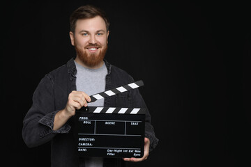 Making movie. Smiling man with clapperboard on black background. Space for text
