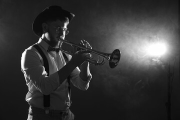 Professional musician playing trumpet on dark background with smoke, space for text. Black and...