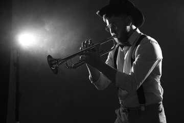 Professional musician playing trumpet on dark background with smoke, space for text. Black and...