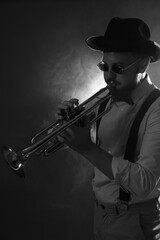 Professional musician playing trumpet on dark background with smoke. Black and white effect