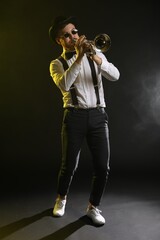 Professional musician playing trumpet on black background in color lights