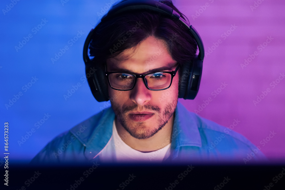 Poster this image shows a young man wearing headphones and glasses while looking intently at a computer scr