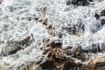 Obraz premium Beach water hitting the dark rocks.