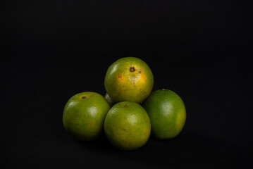 Group of still green oranges on a black background.