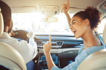 African American woman is enthusiastically singing along to the music in the passenger seat of a...